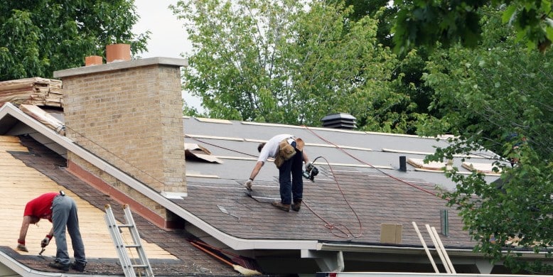 Two roofers installing asphalt shingles on a residential roof during a roof replacement project.