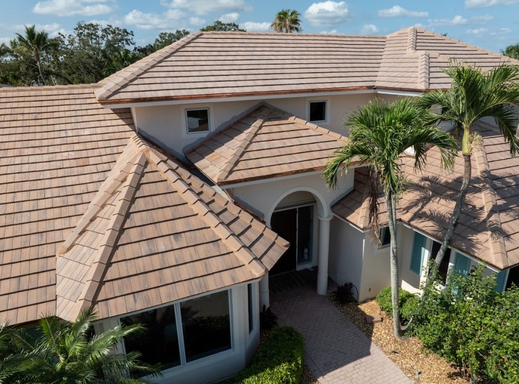 Aerial view of a Florida home with a tan tile roof, multiple roof sections, palm trees, and tropical landscaping.