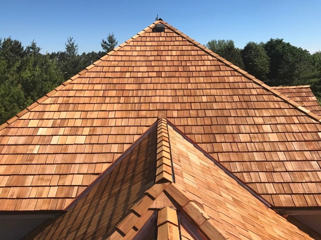 Residential roof covered with natural wood shingles, featuring multiple steep roof sections and ridge caps.