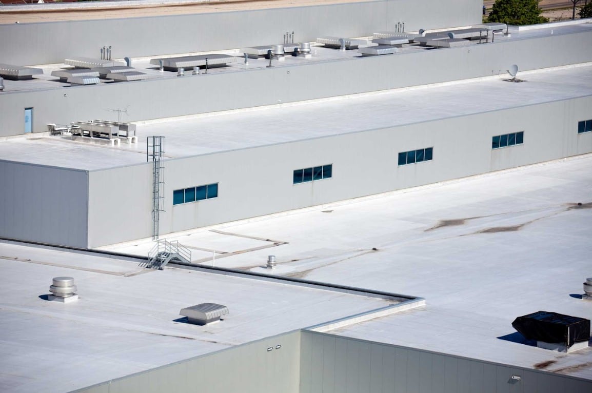 Large commercial building with a white flat roof featuring rooftop vents, skylights, and HVAC equipment.