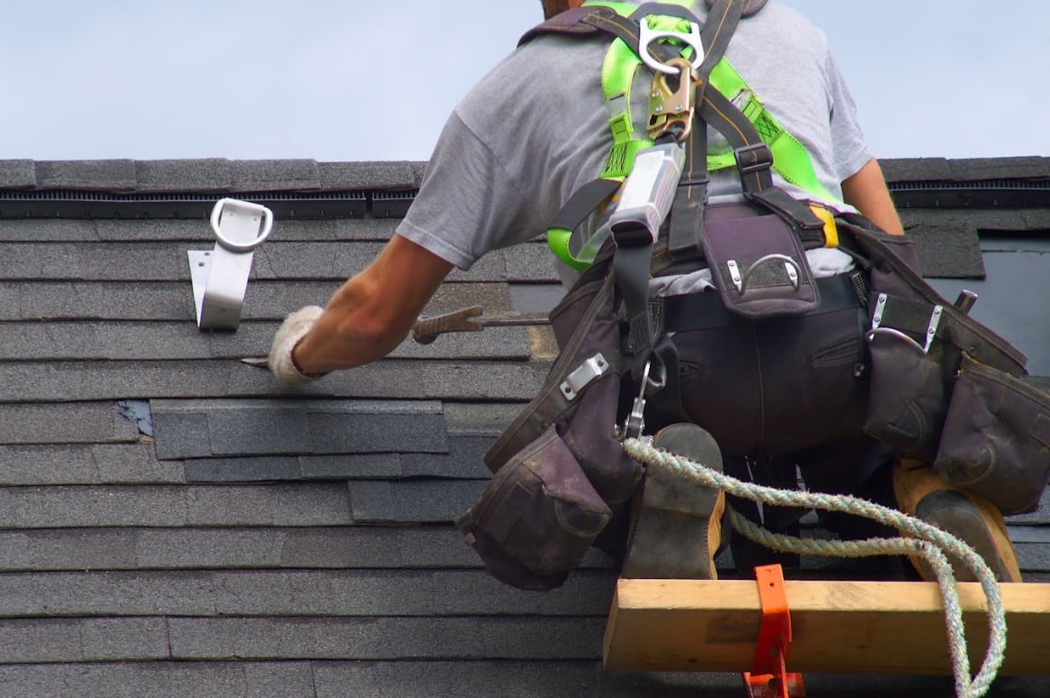 Roofing contractor repairing damaged roof decking beneath asphalt shingles