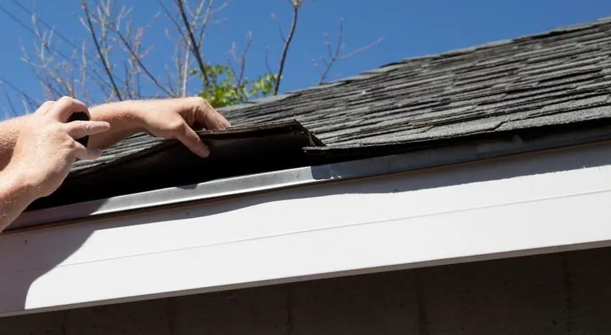 Contractor inspecting a black shingle for roof replacement