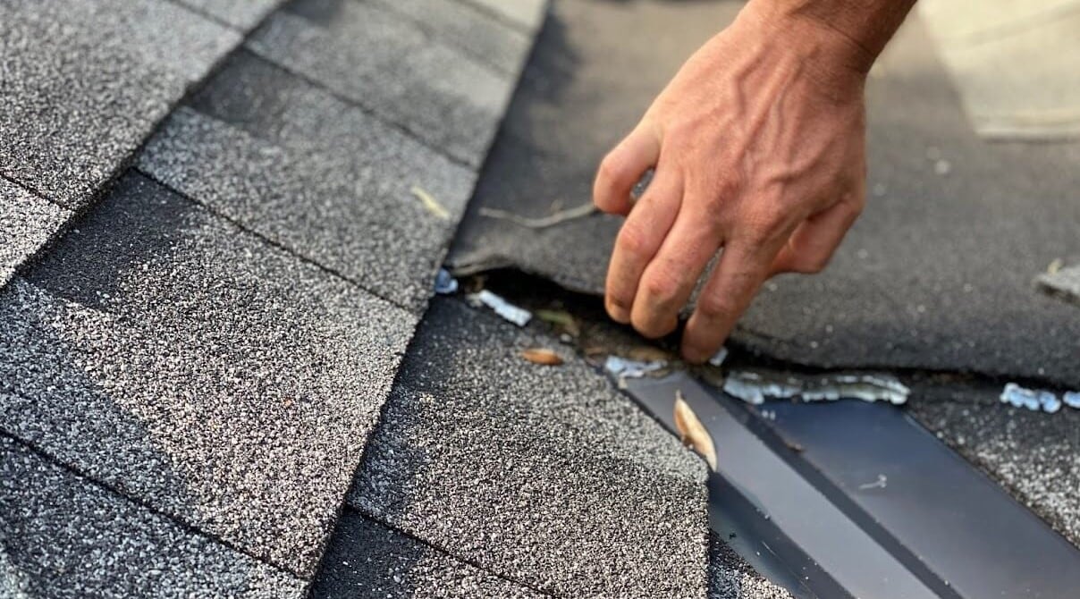 Contractor in a process of roof inspection of a black shingle roof with debris underneath