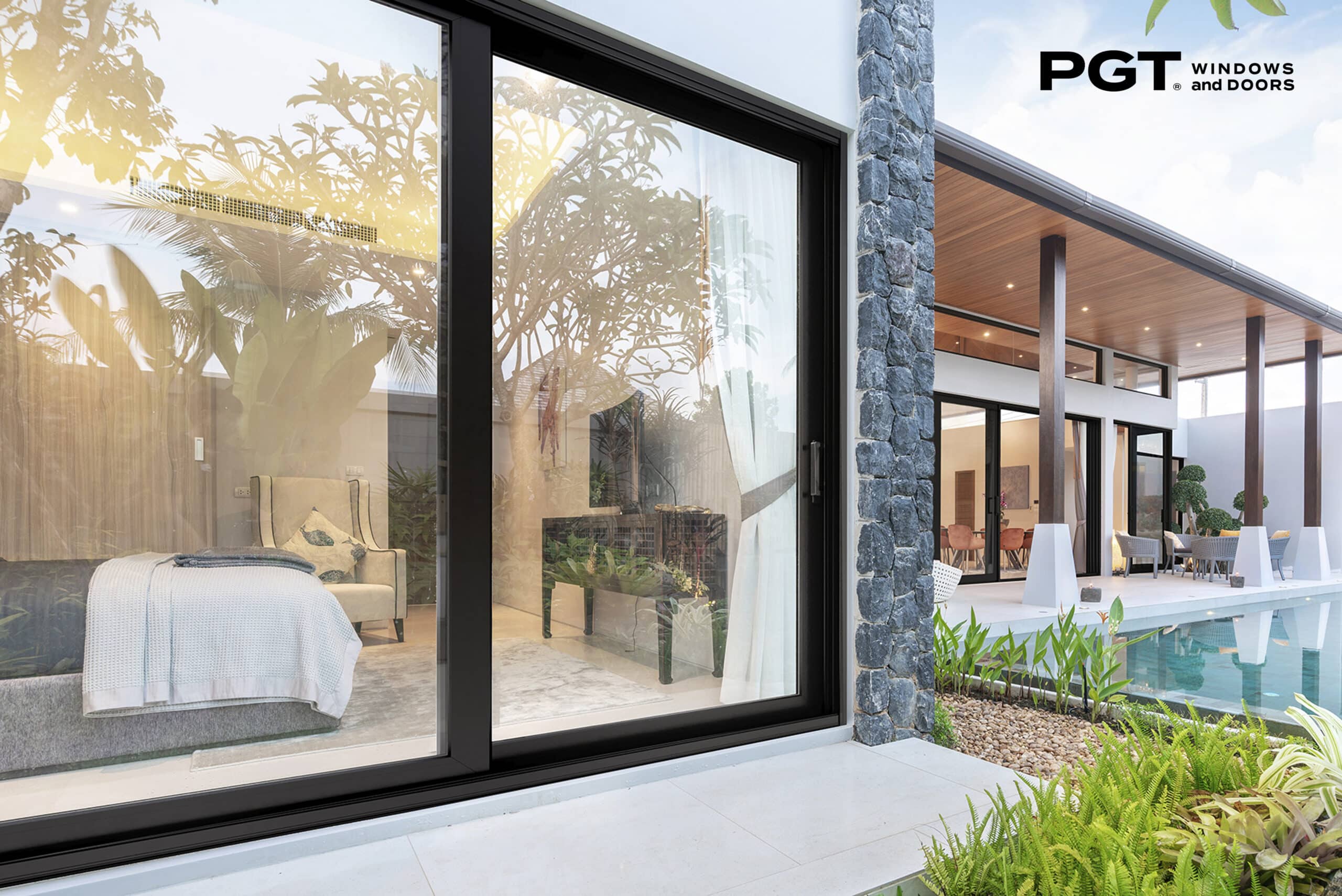 PGT impact sliding glass doors opening from a modern bedroom to a landscaped pool courtyard