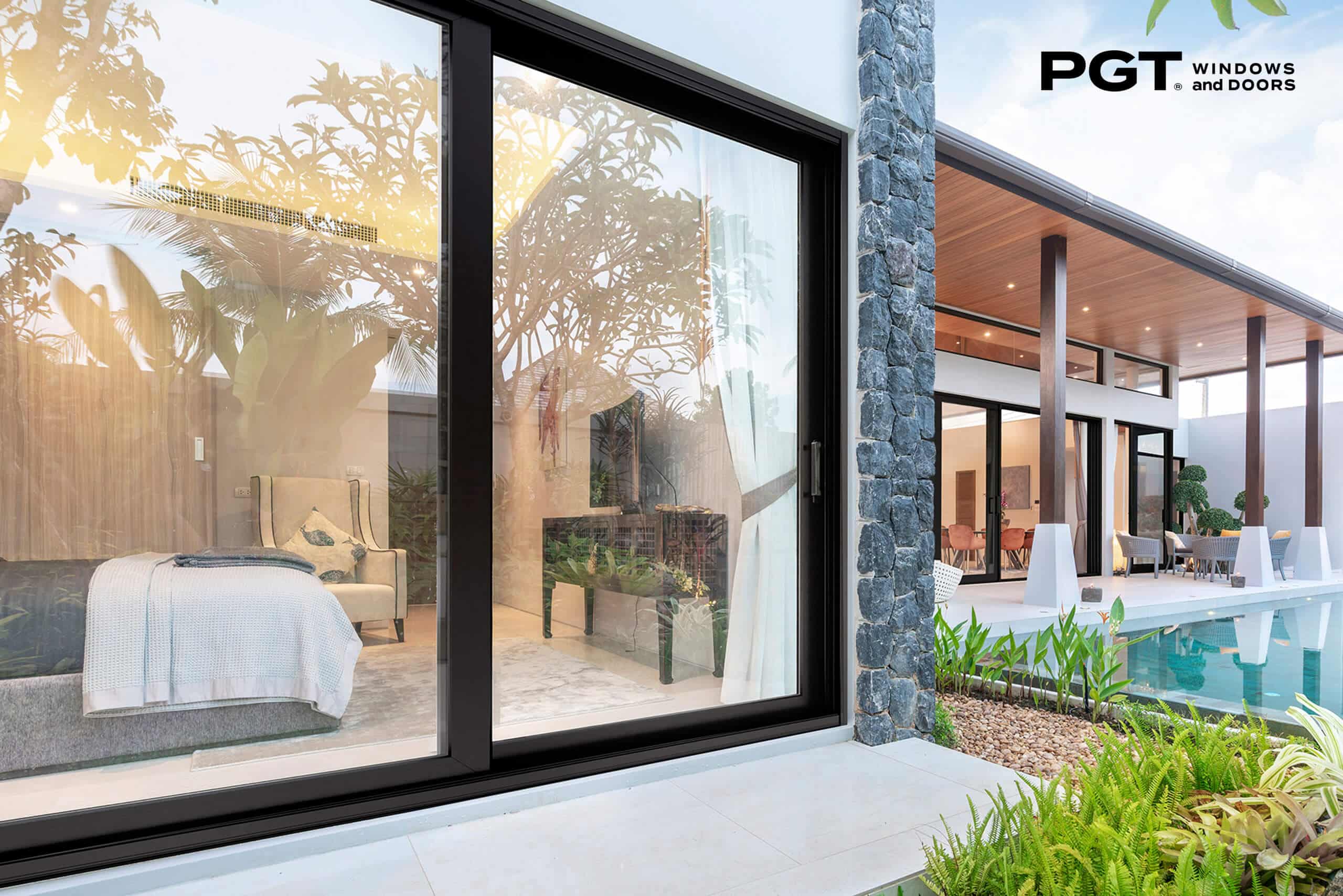 PGT impact sliding glass doors opening from a modern bedroom to a landscaped pool courtyard