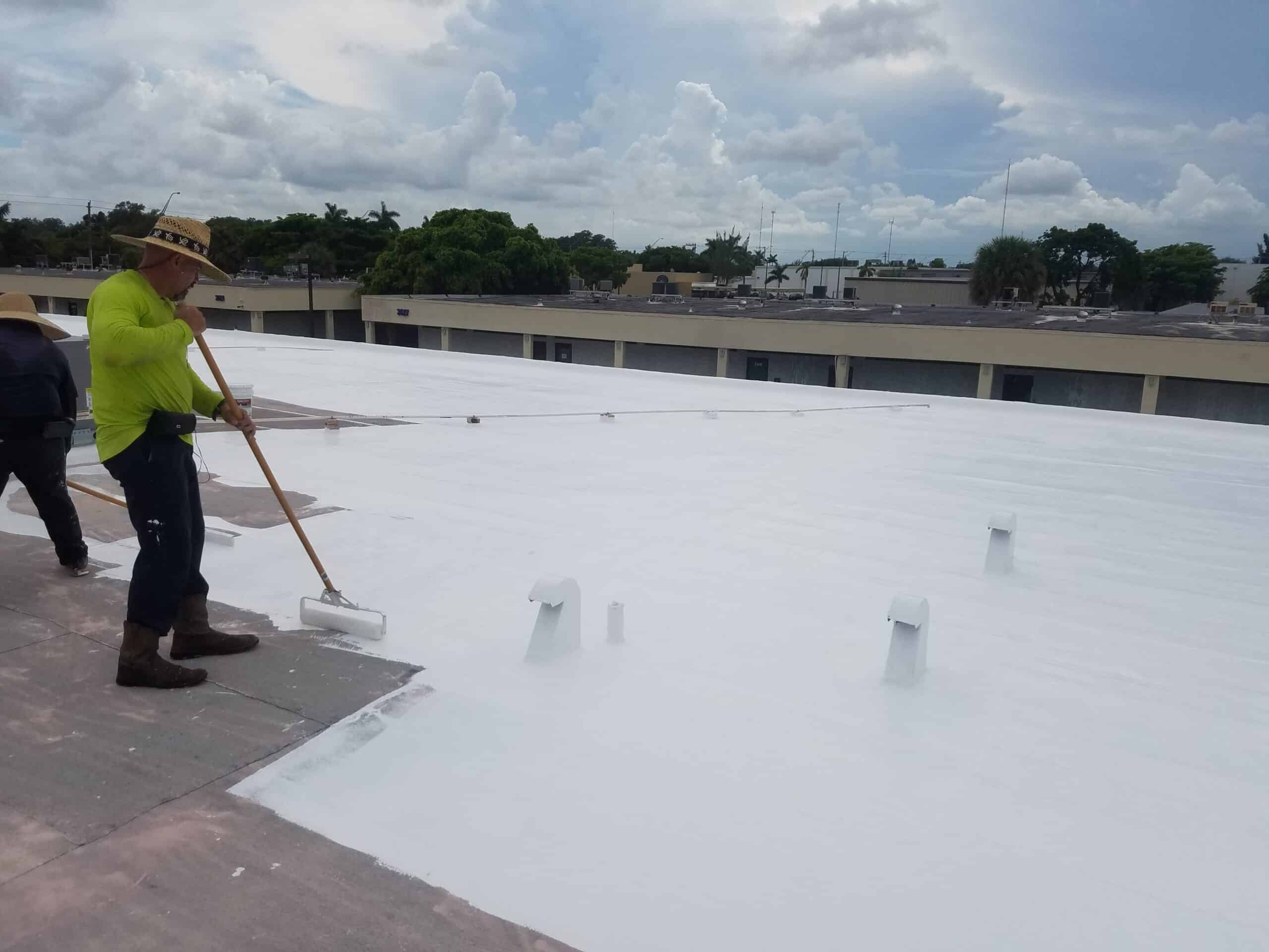 Worker applying white reflective sealant coating to a flat commercial roof.