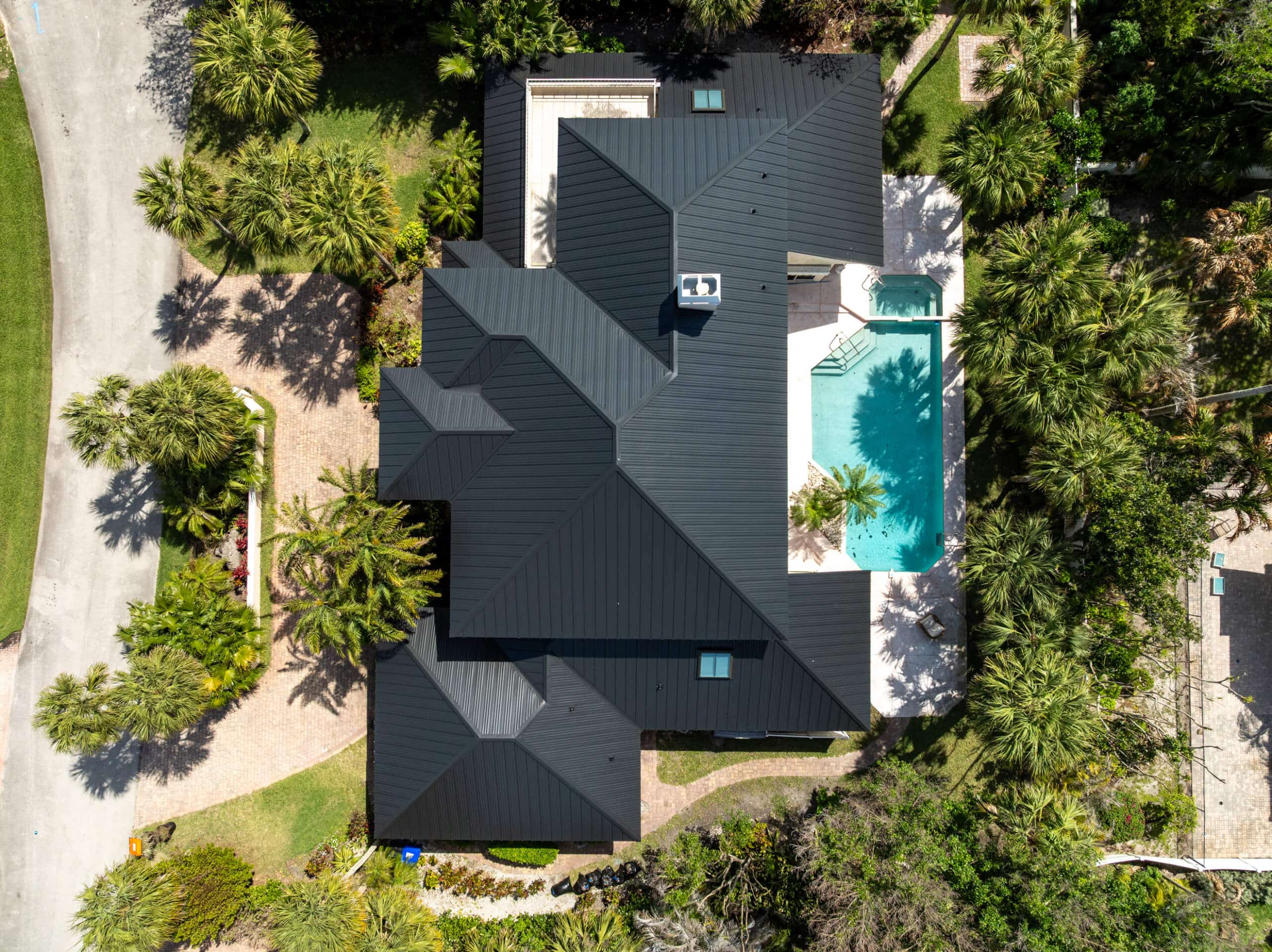 Aerial view of a completed black metal roof replacement on a Florida home with a backyard pool