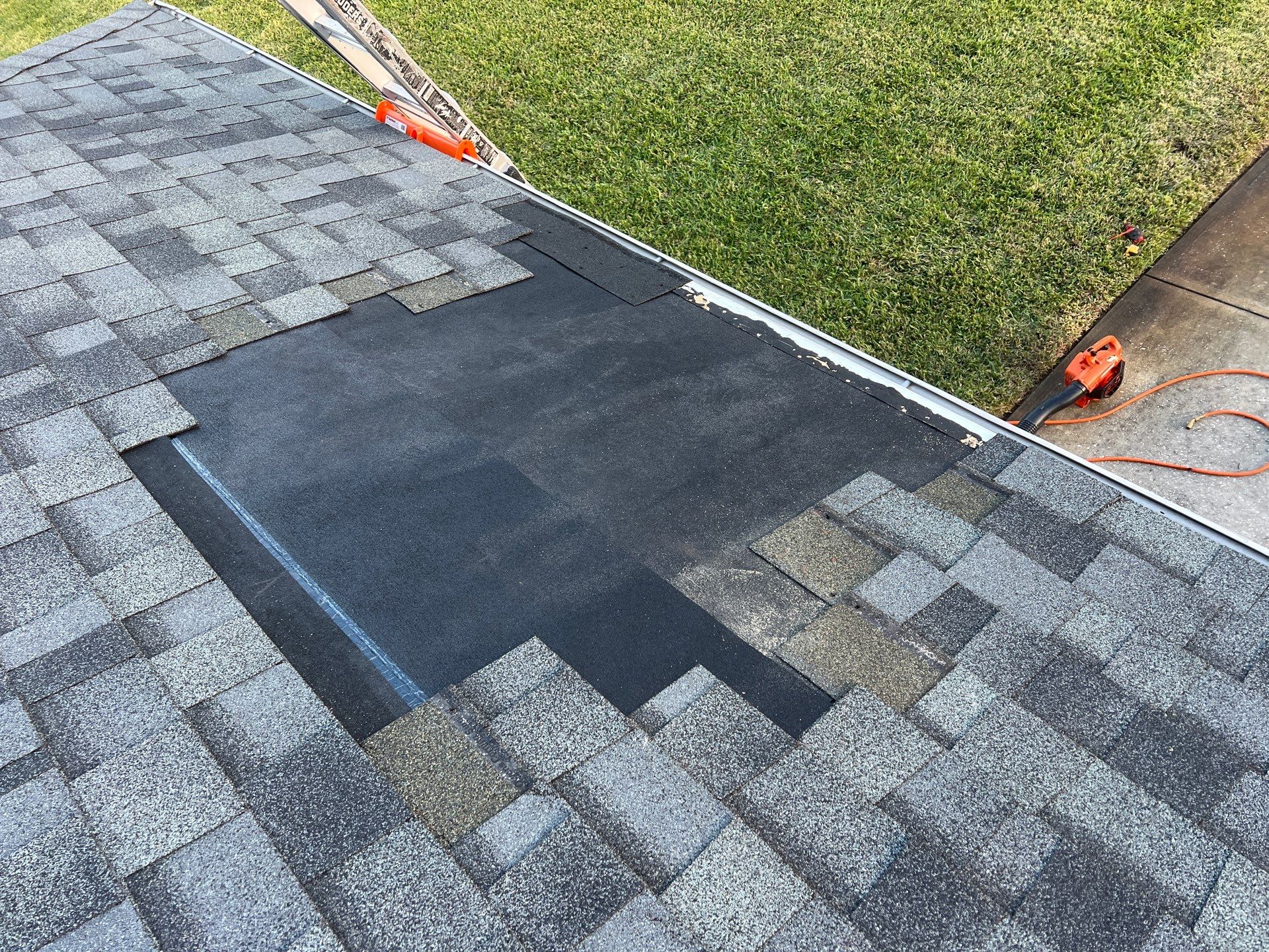 Close-up view of a worker repairing dark asphalt roof shingles along the edge of a roof.